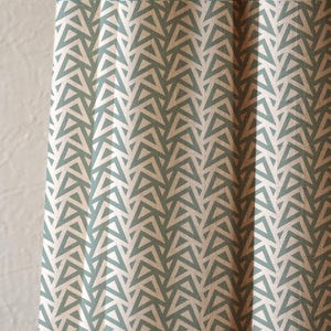 May include: Close-up of a fabric with a repeating geometric pattern. The design features rows of light blue triangles against a cream-colored background. The fabric is folded, creating vertical lines and shadows that add depth to the design. The overall aesthetic is modern and minimalist.