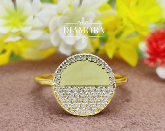 Puede incluir: Un anillo de oro con un diseño de medio círculo. La mitad superior del círculo es de oro liso, mientras que la mitad inferior está cubierta de pequeñas piedras transparentes.