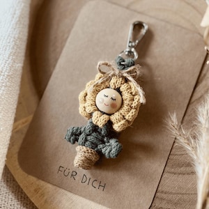 Könnte beinhalten: Ein gelber und grüner gehäkelter Sonnenblumen-Schlüsselanhänger mit einem Holzgesicht und dem Text "Für Dich" auf einer braunen Karte.