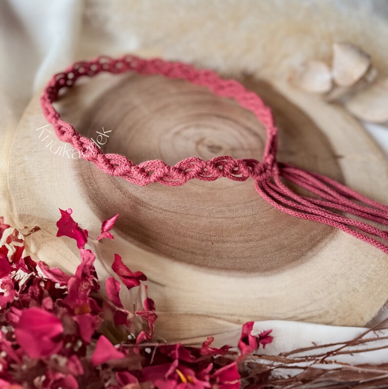 May include: A pink macrame bracelet with a tassel. The bracelet is made with a knotted cord and has a simple design.