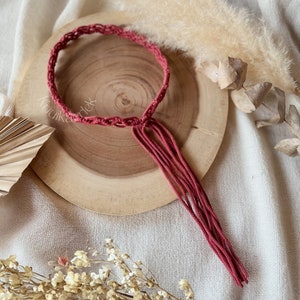May include: A red macrame cord necklace with a tassel. The necklace is on a wooden surface.