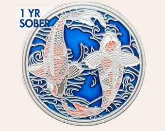 Op de afbeelding: Een ronde, zilverkleurige munt met een blauwe achtergrond met twee koi-karpers in een yin-yang-ontwerp. De vissen zijn wit en oranje, met ingewikkelde details. De tekst "1 YR SOBER" staat in een wit kader linksboven.