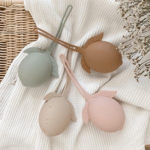 May include: Four silicone lemon-shaped teethers in different colors: green, brown, beige, and pink. Each teether has a loop handle for easy gripping.