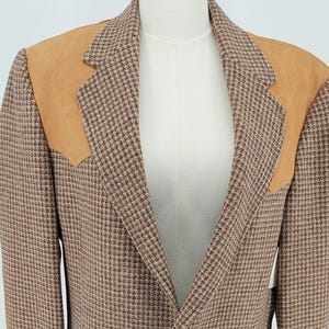 May include: A brown tweed blazer with tan suede shoulder patches. The jacket has a classic houndstooth pattern, two front pockets, and brown buttons. The blazer is displayed on a mannequin.