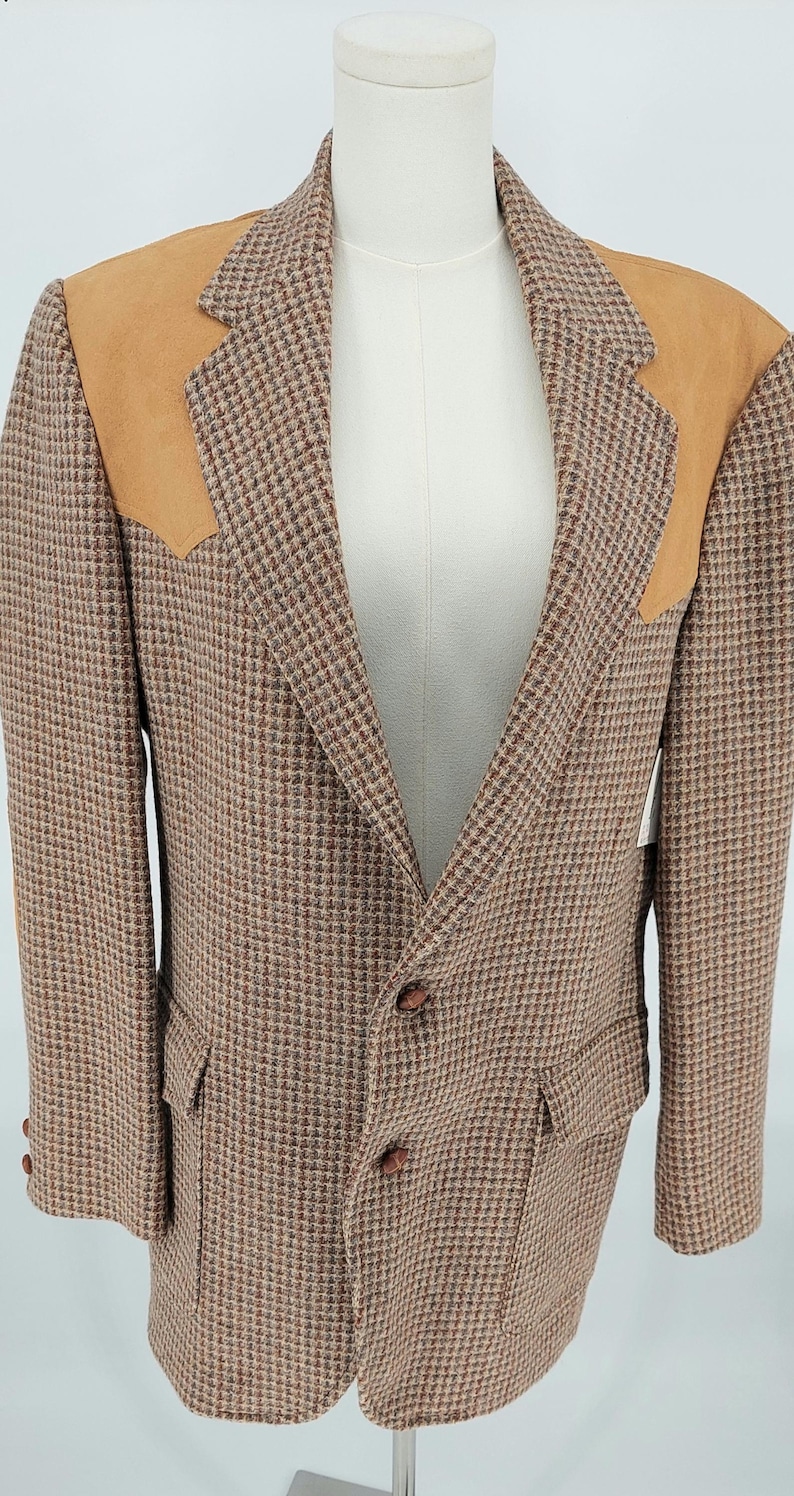 Peut inclure: Un blazer en tweed marron avec des empi&egrave;cements d'&eacute;paule en daim beige. La veste pr&eacute;sente un motif pied-de-poule classique, deux poches avant et des boutons marron. Le blazer est pr&eacute;sent&eacute; sur un mannequin.