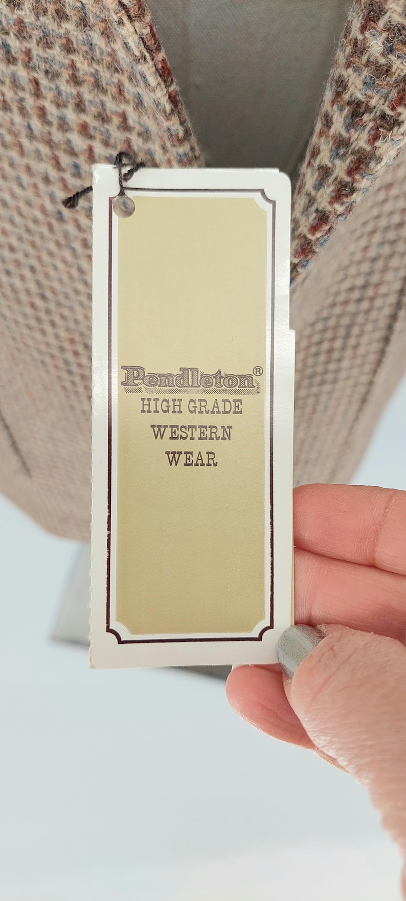 Peut inclure: Une &eacute;tiquette de produit Pendleton, avec le nom de la marque et le texte "HIGH GRADE WESTERN WEAR". L'&eacute;tiquette est de couleur cr&egrave;me avec une bordure fonc&eacute;e et est attach&eacute;e &agrave; un tissu &agrave; motifs.