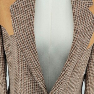 Peut inclure: Blazer en tweed avec des tons marron, beige et rouge. Le blazer pr&eacute;sente un motif pied-de-poule classique et des empi&egrave;cements d'&eacute;paules en daim beige. Il comporte deux poches avant et une fermeture &agrave; deux boutons.