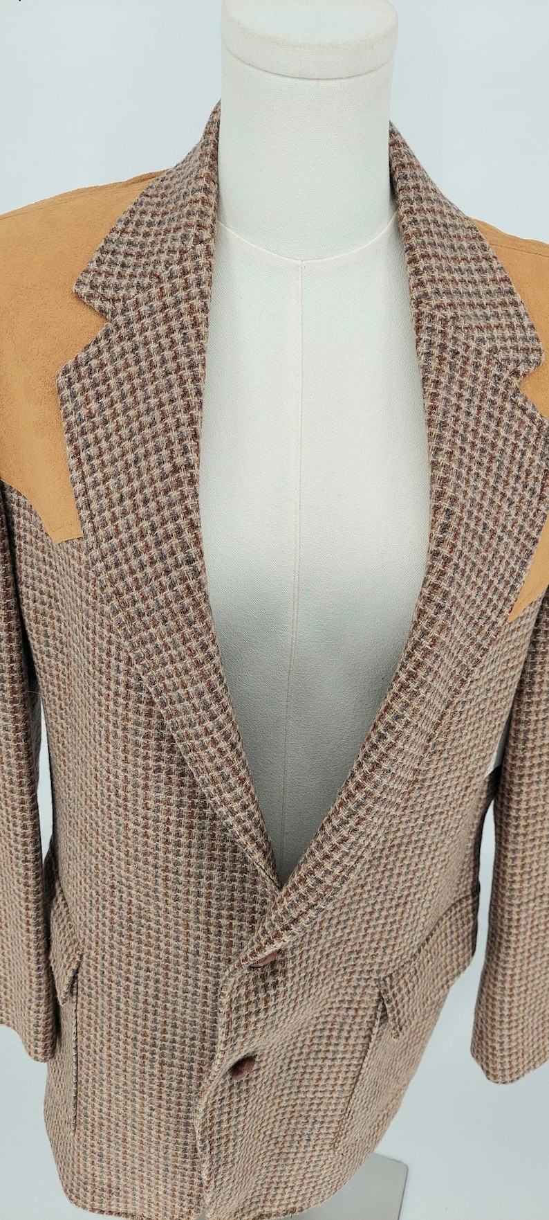 Peut inclure: Blazer en tweed avec des tons marron, beige et rouge. Le blazer pr&eacute;sente un motif pied-de-poule classique et des empi&egrave;cements d'&eacute;paules en daim beige. Il comporte deux poches avant et une fermeture &agrave; deux boutons.