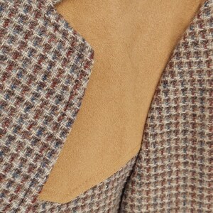 Peut inclure: Gros plan d'un blazer en tweed avec un empi&egrave;cement d'&eacute;paule en daim beige. Le tissu tweed pr&eacute;sente un motif de fils marron, bleus et rouges. Le blazer a un design classique et ajust&eacute;.