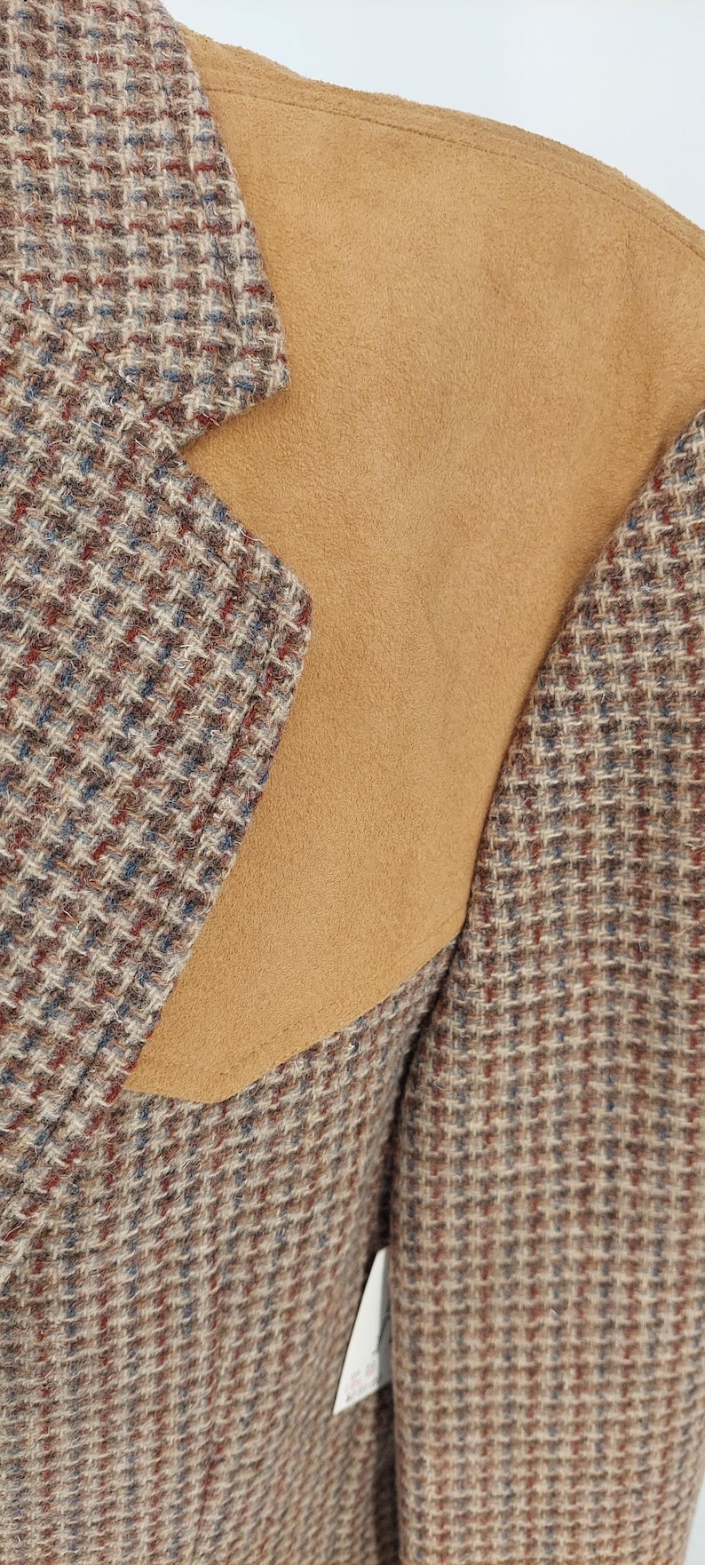 Peut inclure: Gros plan d'un blazer en tweed avec un empi&egrave;cement d'&eacute;paule en daim beige. Le tissu tweed pr&eacute;sente un motif de fils marron, bleus et rouges. Le blazer a un design classique et ajust&eacute;.