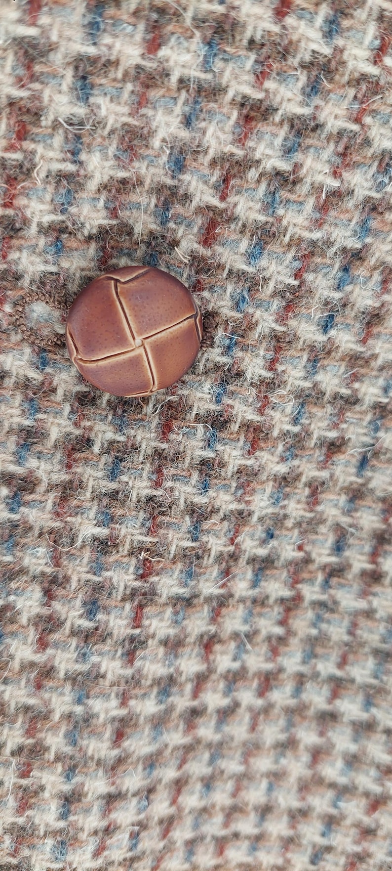 Peut inclure: Gros plan d'un bouton rond marron avec un motif en point de croix. Le bouton est pos&eacute; sur un tissu tweed textur&eacute; aux tons marron, bleu et rouge.