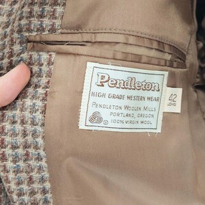 Peut inclure: Gros plan de l'int&eacute;rieur d'une veste Pendleton en laine marron. La doublure est de couleur beige uni. Une &eacute;tiquette indique "Pendleton High Grade Western Wear" avec la taille "42 Long".