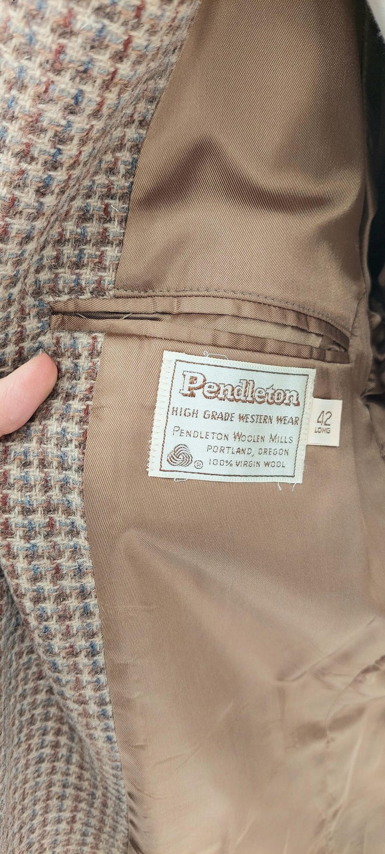 Peut inclure: Gros plan de l'int&eacute;rieur d'une veste Pendleton en laine marron. La doublure est de couleur beige uni. Une &eacute;tiquette indique "Pendleton High Grade Western Wear" avec la taille "42 Long".