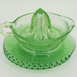May include: A vintage green glass citrus juicer set. The set includes a reamer, a bowl with a handle, and a matching saucer. The glass has a ribbed design. The juicer is a light, translucent green color.