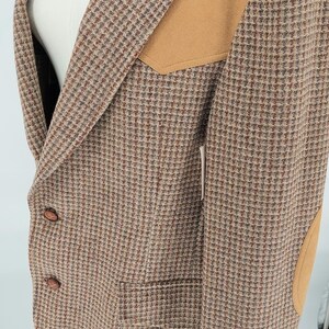 Peut inclure: Blazer en tweed marron avec des empi&egrave;cements d'&eacute;paule et de coude en daim beige. Le blazer pr&eacute;sente un motif pied-de-poule classique, deux poches avant et des boutons marron. Le v&ecirc;tement est pr&eacute;sent&eacute; sur un mannequin.