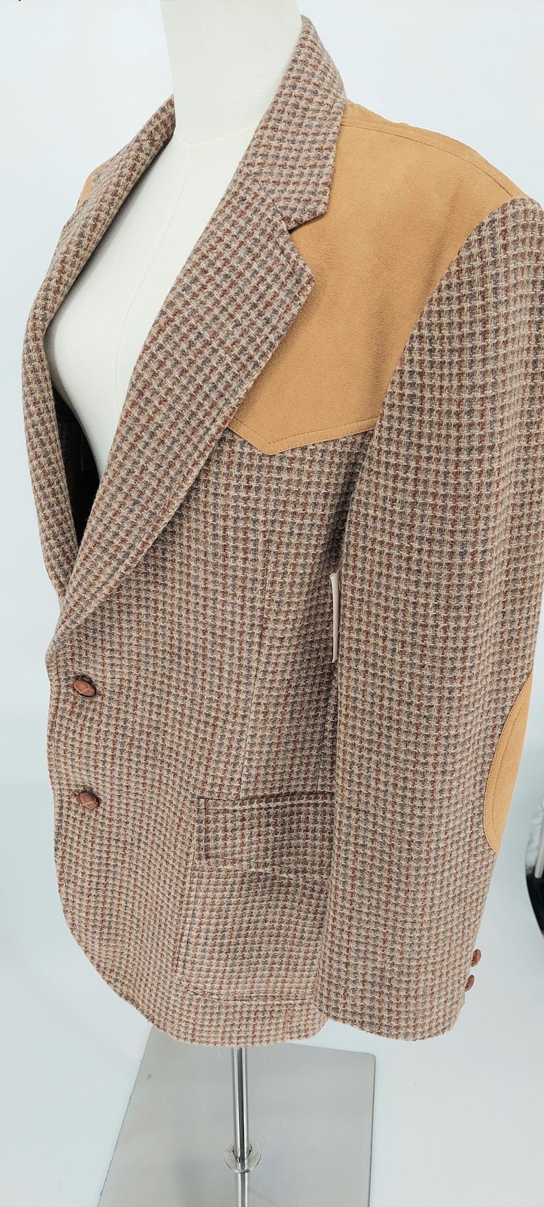Peut inclure: Blazer en tweed marron avec des empi&egrave;cements d'&eacute;paule et de coude en daim beige. Le blazer pr&eacute;sente un motif pied-de-poule classique, deux poches avant et des boutons marron. Le v&ecirc;tement est pr&eacute;sent&eacute; sur un mannequin.