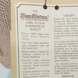 Peut inclure: Gros plan sur une &eacute;tiquette Pendleton, avec le logo de la marque et le texte garantissant la qualit&eacute;. L'&eacute;tiquette est attach&eacute;e &agrave; un tissu &agrave; motifs, soulignant l'engagement de la marque envers la qualit&eacute; et le design.