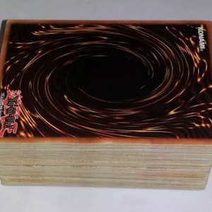 May include: A stack of black and gold Yu-Gi-Oh! trading cards with a swirling black vortex design and the word "KONAMI" printed on the top right corner.