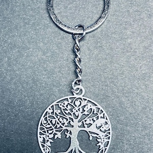 Può includere: Portachiavi in ​​argento a forma di albero della vita con un design circolare e dettagli intricati. Il portachiavi presenta una catena attorcigliata e un anello d'argento.