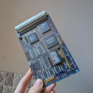 Può includere: Una scheda di circuito blu con più circuiti integrati, connettori e componenti elettronici. La scheda presenta il testo "ALTERA" e "Act". La scheda è tenuta in mano.