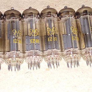 Pode incluir: Uma fileira de onze válvulas de vácuo EZ 81 vintage. Cada tubo tem um corpo de vidro transparente, um topo escuro e uma base com vários pinos. Os tubos têm texto amarelo que diz "EZ 81" e um logotipo.