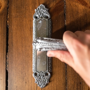 Può includere: Una maniglia per porta argentata con un designo ornato, montata su una porta in legno.
