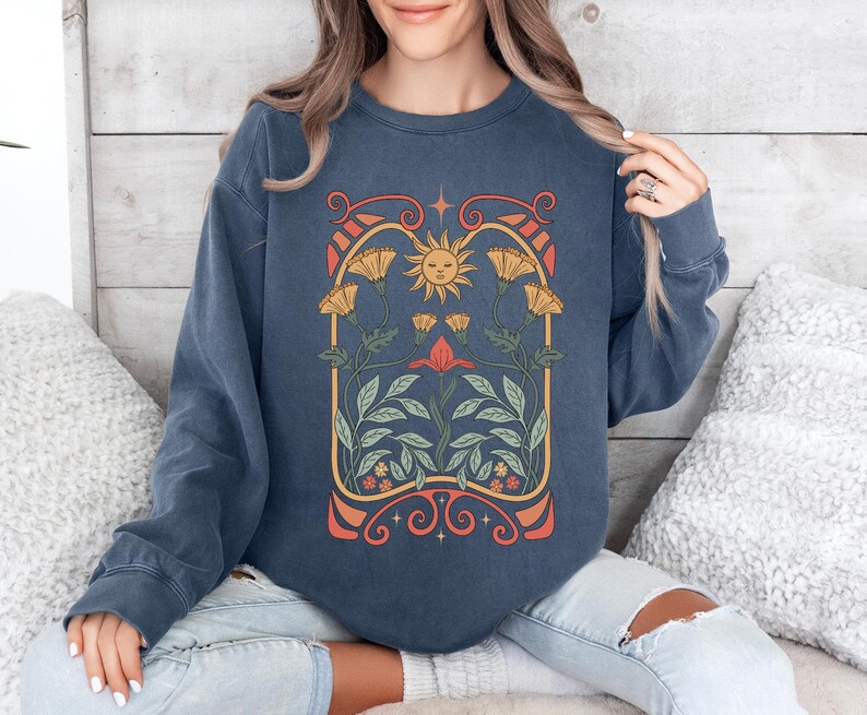 Op de afbeelding: Een marineblauw sweatshirt met een vintage-ge&iuml;nspireerde afbeelding van een zon en bloemen in een bloemvormige boog. De afbeelding is in tinten geel, oranje, rood en groen.