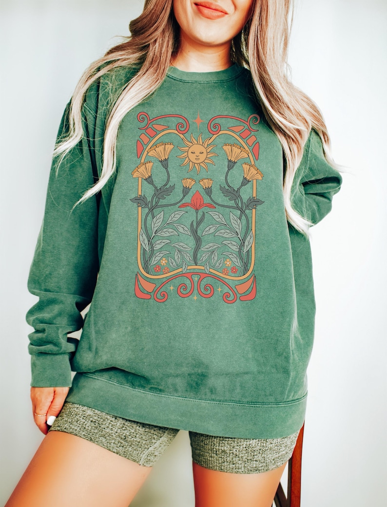 Op de afbeelding: Een groen sweatshirt met een vintage-stijl grafische afbeelding van een zon en bloemen. De afbeelding is in tinten oranje, geel, rood en groen.