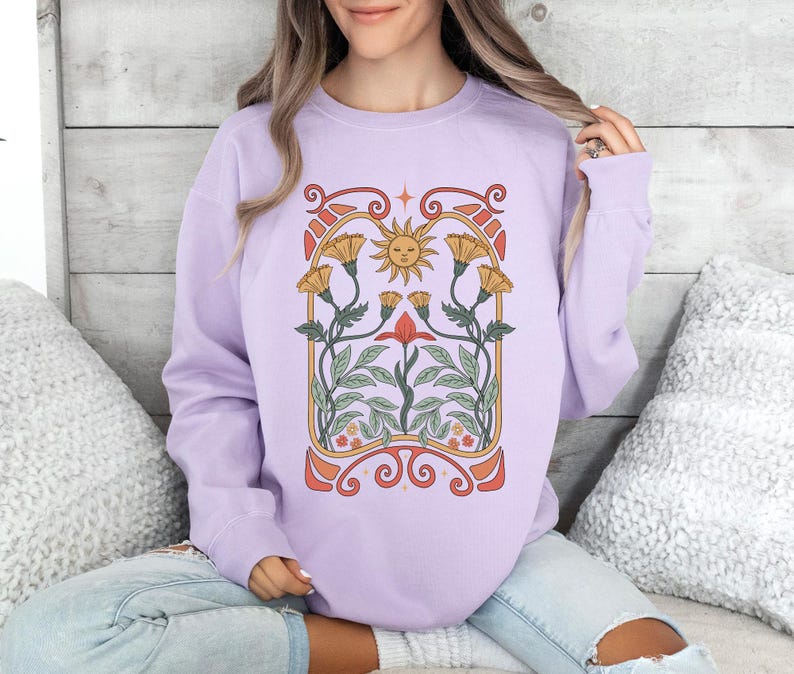 Op de afbeelding: Een lavendelkleurig sweatshirt met een grafische print van een zon en bloemen in een vintage art nouveau-stijl.