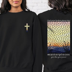 May include: Black sweatshirt with a cross on the front and the text "God turns broken pieces into masterpieces give him your pieces" on the back. The back design features a stained glass style sunset.