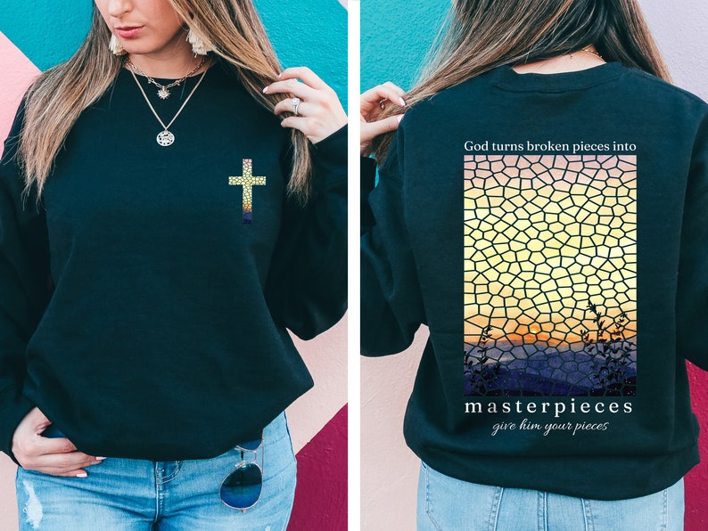 May include: Black sweatshirt with a gold cross on the front and a stained glass sunset design on the back. The back design includes the text "God turns broken pieces into masterpieces give him your pieces".