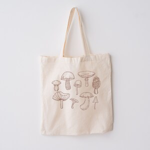 May include: A beige canvas tote bag with a brown line drawing of various mushrooms on the front.