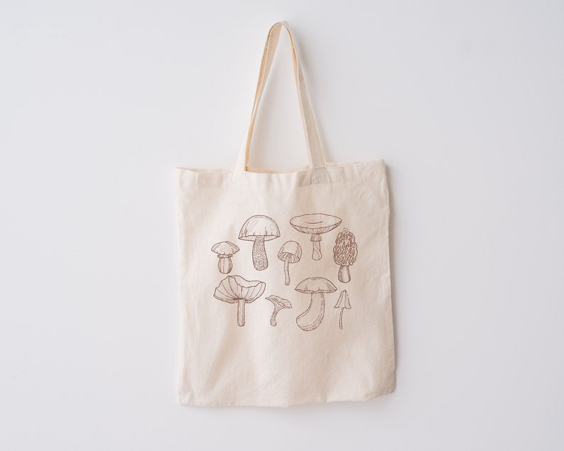 May include: A beige canvas tote bag with a brown line drawing of various mushrooms on the front.