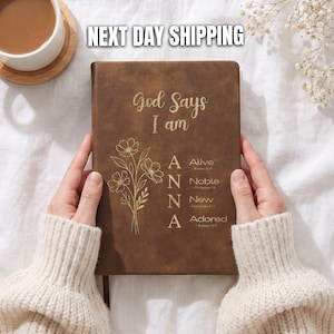 May include: A brown leather-look journal featuring the gold text God Says I am, a floral illustration, and the name ANNA with the words Alive, Noble, New, and Adored, each accompanied by a Bible verse reference printed on the front cover.