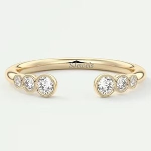 Puede incluir: Un anillo de oro con cinco pequeños diamantes redondos engastados en una banda curva. El anillo está abierto por un lado, creando un diseño único y moderno. La inscripción "S Jewels" es visible en la banda.