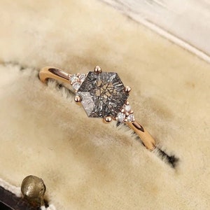 May include: A rose gold engagement ring featuring a hexagonal grey diamond with smaller diamonds set around it.