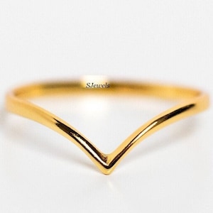Può includere: Un anello a forma di V color oro. L'anello ha una superficie liscia e lucida e un design minimalista. L'anello è un gioiello delicato, perfetto per l'uso quotidiano. Il testo "SJewels" è visibile in alto a destra.
