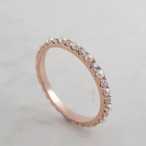 Puede incluir: Un delicado anillo de banda de oro rosa con pequeñas perlas blancas y diamantes alternados.