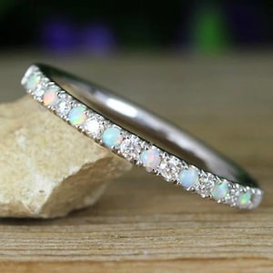 May include: A delicate silver band ring with a row of alternating white opals and diamonds.