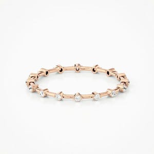 Peut inclure: Une délicate bande en or rose avec une rangée de petits diamants ronds sertis dans un design minimaliste.