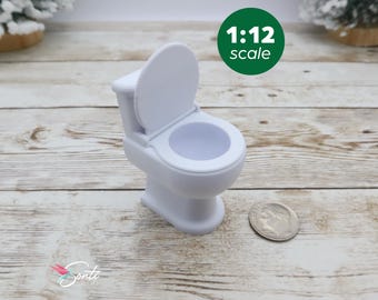 May include: White plastic miniature toilet with a closed lid, 1:12 scale. The toilet is sitting on a light brown wooden surface.