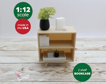 May include: A miniature 2-shelf bookcase in a light wood finish, with a small plant, books, and decorative items. The bookcase is 1:12 scale and made in the USA. The image also includes the text "2 shelf BOOKCASE".