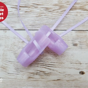 May include: Two lilac ballet shoes with ribbons, set on a light wood surface. The shoes have white straps and a satin finish. The text "Purple Ballet Shoes" is in a red circle.