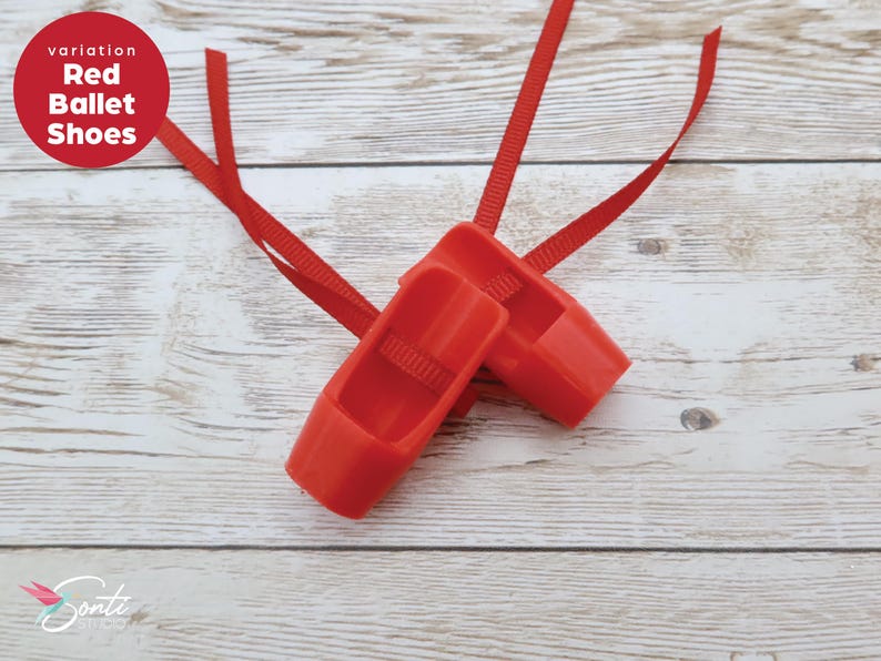 May include: Two bright red ballet shoes with matching ribbons, resting on a light wood-grain surface. The shoes are a vibrant red, and the ribbons are tied in a bow. The text "Red Ballet Shoes" is in a red circle.