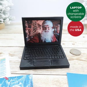 May include: A black laptop with a screen showing a photo of Santa Claus. The laptop is made of plastic and has a keyboard and a touchpad. The laptop is sitting on a wooden table. The text "LAPTOP with changeable screens made in the USA" is visible in the image.