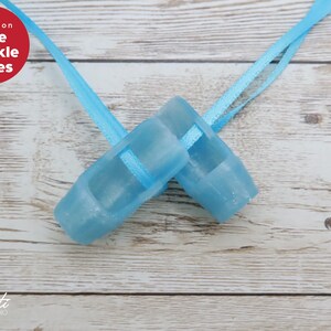 May include: Two light blue sparkle shoes with matching ribbons are displayed on a light wood surface. The shoes are small, possibly for a child or doll. The text "Blue Sparkle Shoes" is in a red circle.