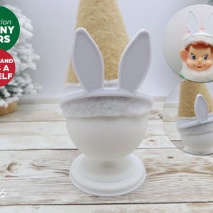 May include: White bunny ears headband for a 10 inch elf. The headband is made of white felt and has two white bunny ears. The headband is shown on a white elf head.