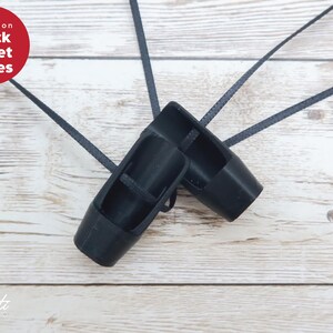 May include: A pair of black ballet shoes with long black ribbons, on a light wood grain surface. The shoes are a solid black colour and have a classic ballet slipper design. The text "variation Black Ballet Shoes" is in a red circle.