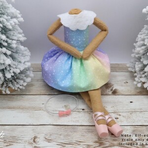 May include: A handmade doll with a rainbow-coloured skirt and a white collar. The doll has tan arms and legs, and is wearing pink ballet shoes. A clear headband with a pink bow is also included. The doll is a decorative item.