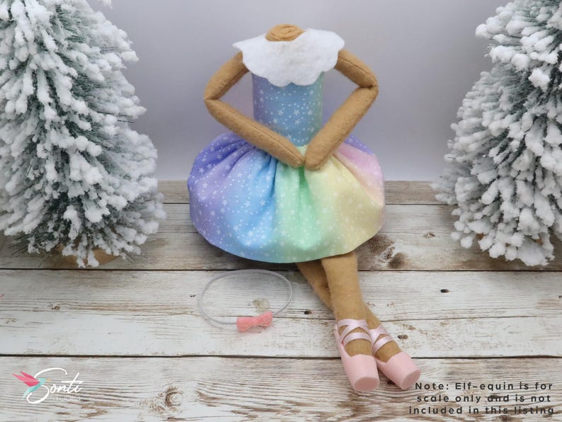 May include: A handmade doll with a rainbow-coloured skirt and a white collar. The doll has tan arms and legs, and is wearing pink ballet shoes. A clear headband with a pink bow is also included. The doll is a decorative item.